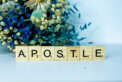 a wooden block spelling apostle next to a bouquet of flowers